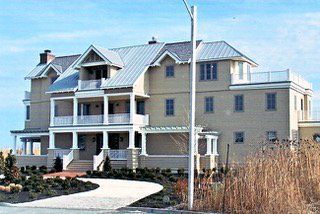Multi-story beige house with white trim, balconies, and a metal roof against a blue sky.