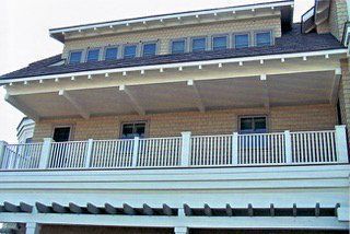 Exterior view of a multi-level house with a deck, white railings, and tan siding.