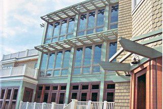 Multi-story building with large windows and a green facade, and a wooden pergola, under a blue sky.