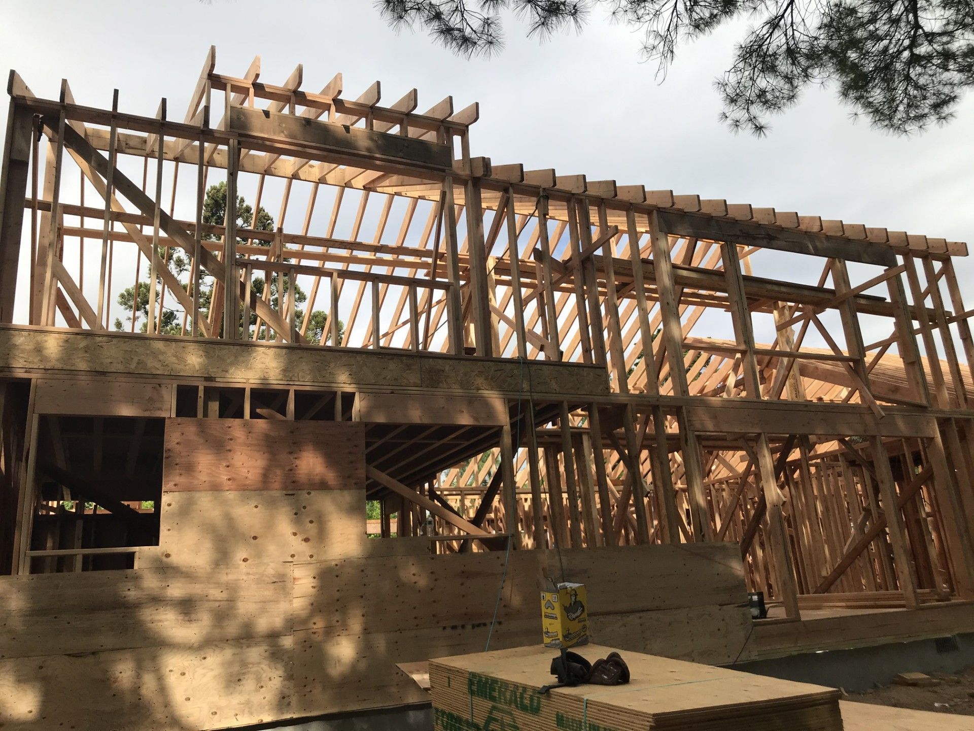 The wood-framed structure of a house under construction, featuring exposed beams and roof rafters against a cloudy sky.
