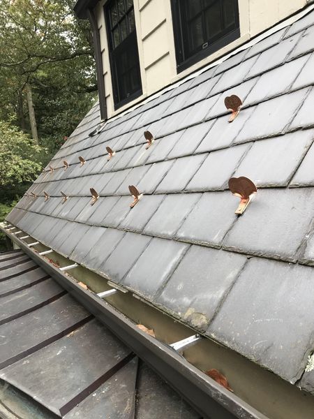 Slate roof with copper hangers along a gutter, a close-up angle.