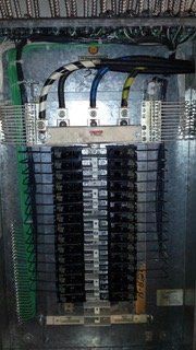 Electrical panel with black circuit breakers, connected wires, and bus bars.