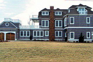 Large gray house with multiple stories, balconies, and a garage; brown lawn in front.