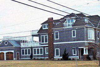 Large grey house with multiple stories, balconies, and a brown brick chimney.