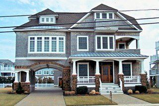 Two-story gray house with archway, porch, and brown roof. Driveway leads under the arch.