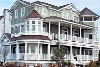 Multi-story light green house with white trim, multiple balconies, and a brown turret.