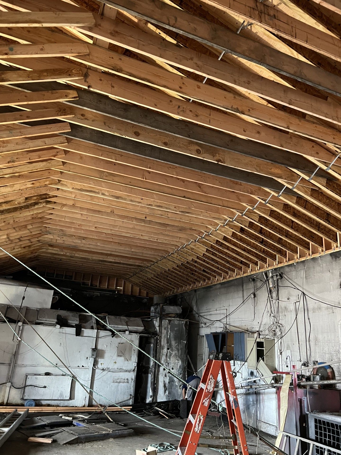 An unfinished interior construction site with exposed wooden roof beams, white walls, and a tall red ladder.