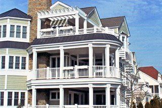 Multi-story house with white balconies, tan siding, and a dark roof.