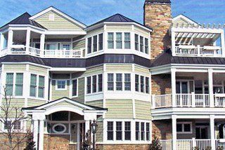 Multi-story house with green siding, multiple balconies, and a stone chimney.