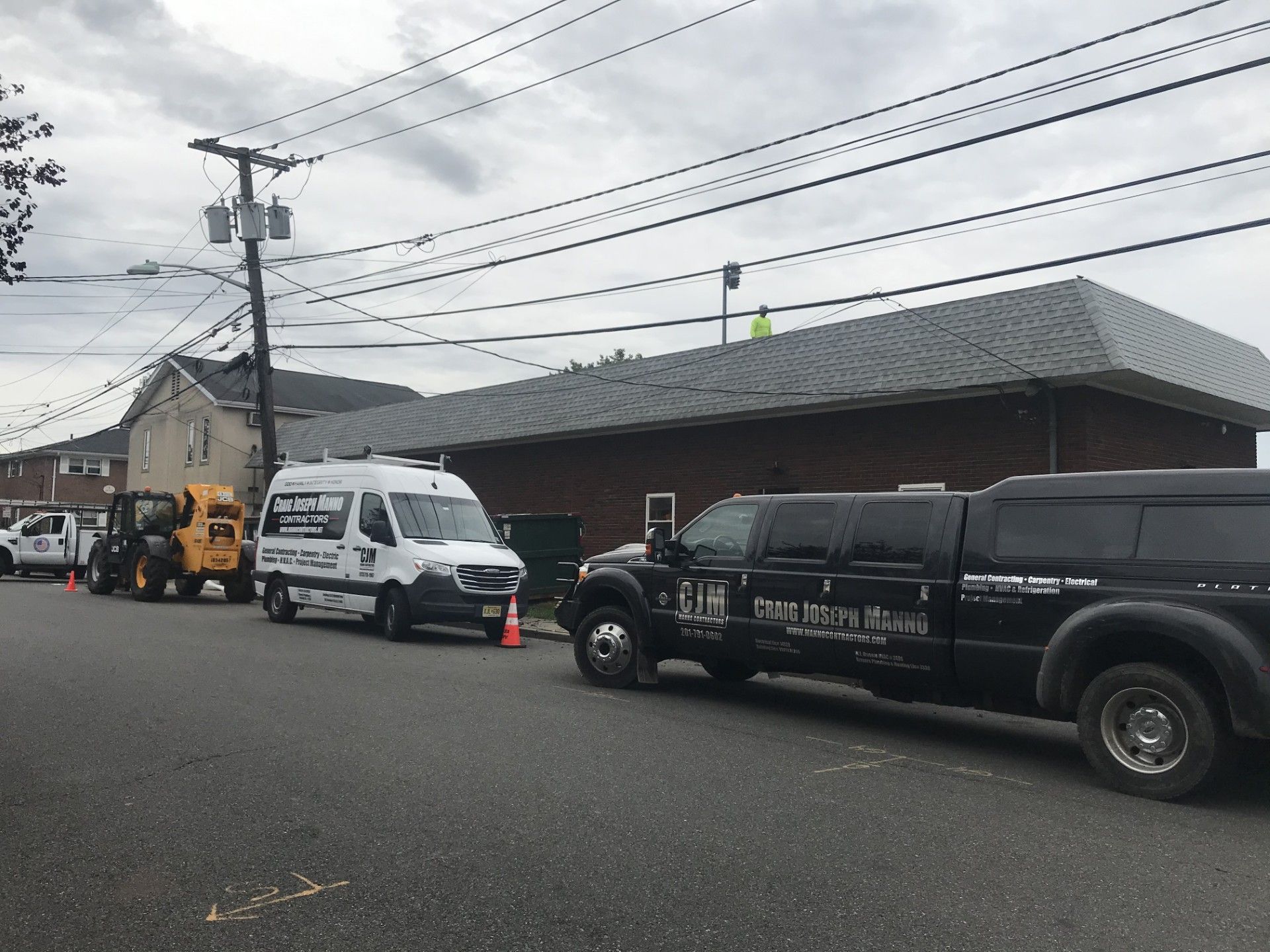A construction crew and vehicles parked in front of a brick building with a gray metal roof.
