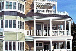 Multi-story house with several white balconies and a pergola. Light green siding and dark roof.