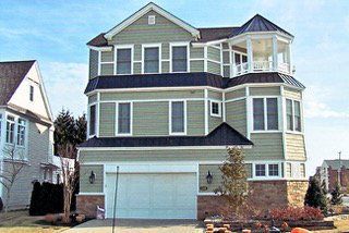 Three-story green house with a turret, white trim, and a garage.