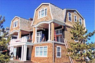 Large multi-story house with cedar shingles and porch under clear blue sky.