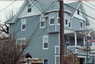 Blue multi-story house with bay window and porch, wires obscure view.