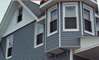 Blue-gray house exterior with white trim. Bay windows and a gabled roof are visible.