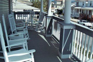 Porch with several white rocking chairs, overlooking a street with houses.