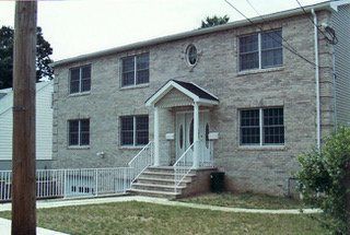 Two-story brick building with multiple windows, a small porch, and a grassy lawn.