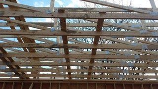 Wooden roof trusses under construction, with a partially framed wall.
