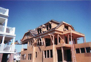 House under construction, unfinished wood structure with a partially built roof, blue sky backdrop.
