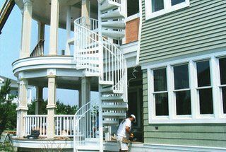White spiral staircase connects a porch and green house. A person stands near the house entrance.