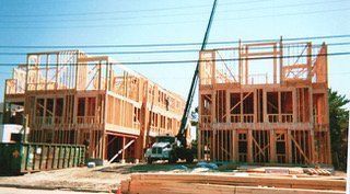 Two-story wooden buildings under construction with a crane and building materials.