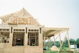 Wooden house under construction; frame visible, roof partially built; exterior, daytime.