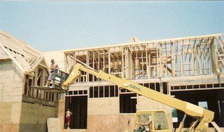 Construction of a house with a yellow boom lift; workers are on the platform.