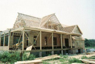 House under construction; wooden frame, open roof, and porch.
