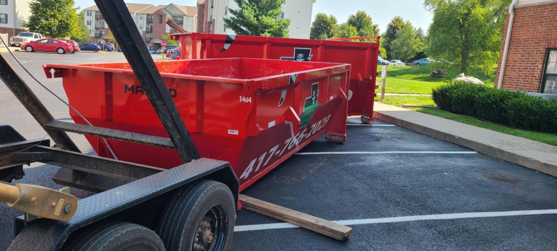 A red dumpster is sitting on top of a trailer in a parking lot.