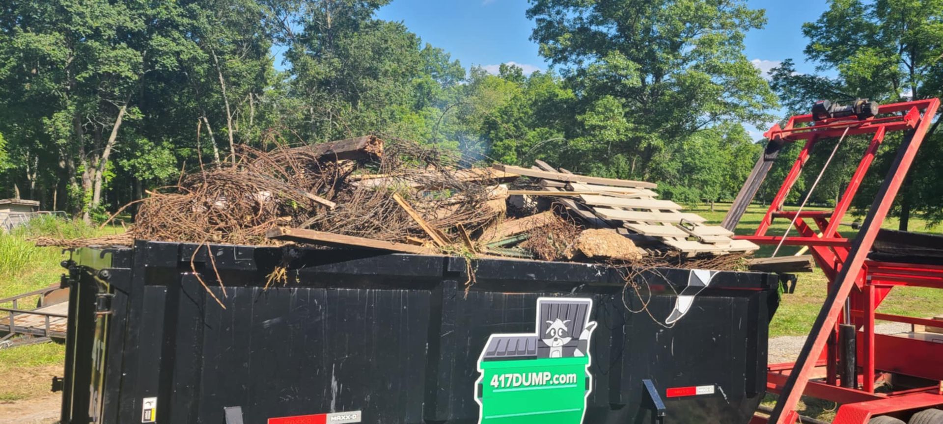 A dumpster filled with wood is sitting next to a red truck.