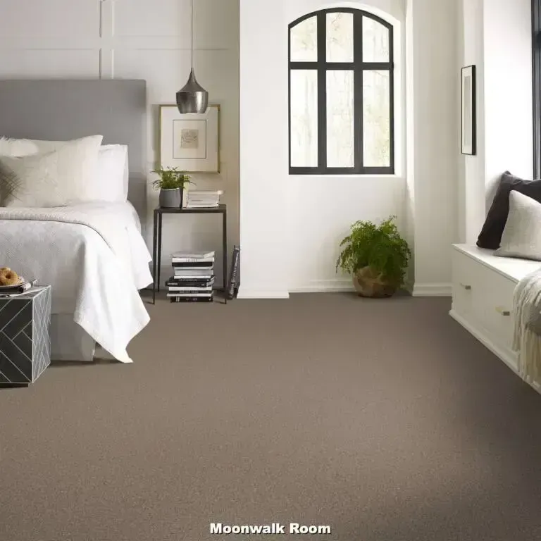 Bedroom with gray carpet, white walls, large window, bed, and small side table.
