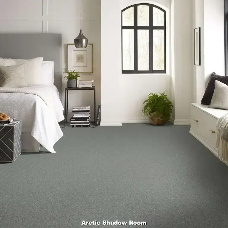Bedroom with gray carpet, a bed, a window, and a small side table.