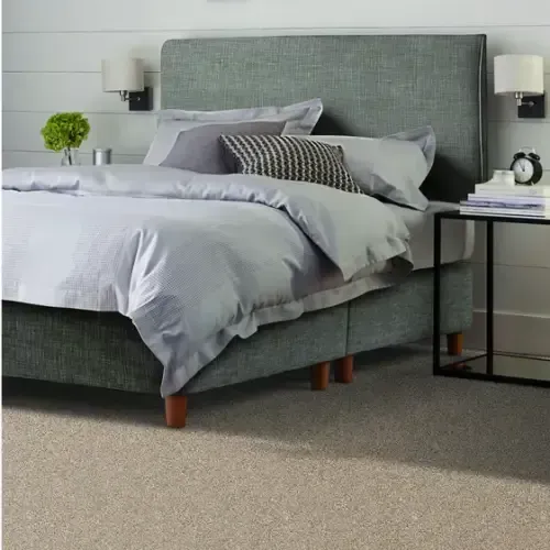 Bedroom with a gray upholstered bed, light blue bedding, two sconces, a side table, and beige carpet.