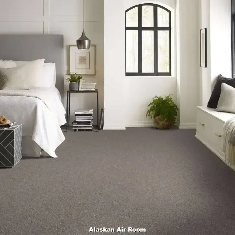 Bedroom with grey carpet, bed, window with black frame, a bench, and a small side table.