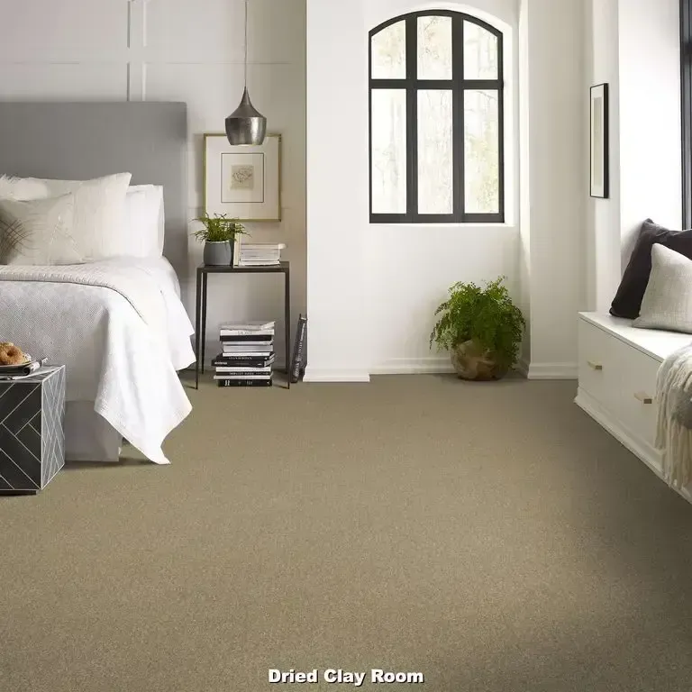 Bedroom with neutral carpet and bed; side table with books, window seat, and potted plant.