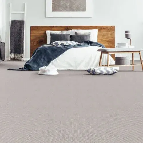 Bedroom with light gray carpet, wooden headboard, white and navy bedding, decorative pillows.