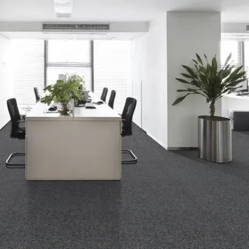 Office interior with a large white desk, black chairs, and a potted plant on dark carpet.