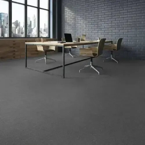 Gray office space with meeting table and chairs; a laptop sits on the table; brick wall and city view in the background.