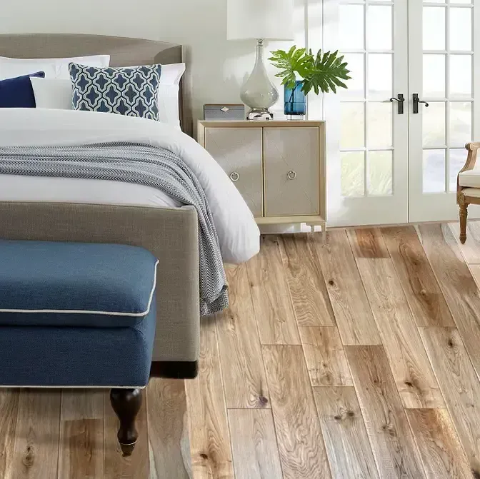 Bedroom with light wood flooring, bed with blue accents, nightstand, and French doors.