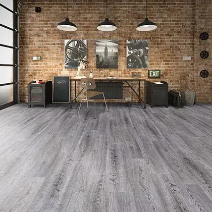 Room with grey wood-look flooring, exposed brick wall, and industrial decor; desk and chairs are present.