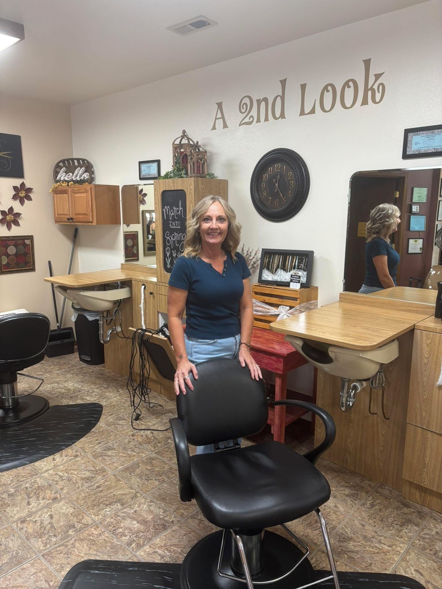Salon interior with a smiling woman standing behind a black chair, “A 2nd Look” sign on the wall.
