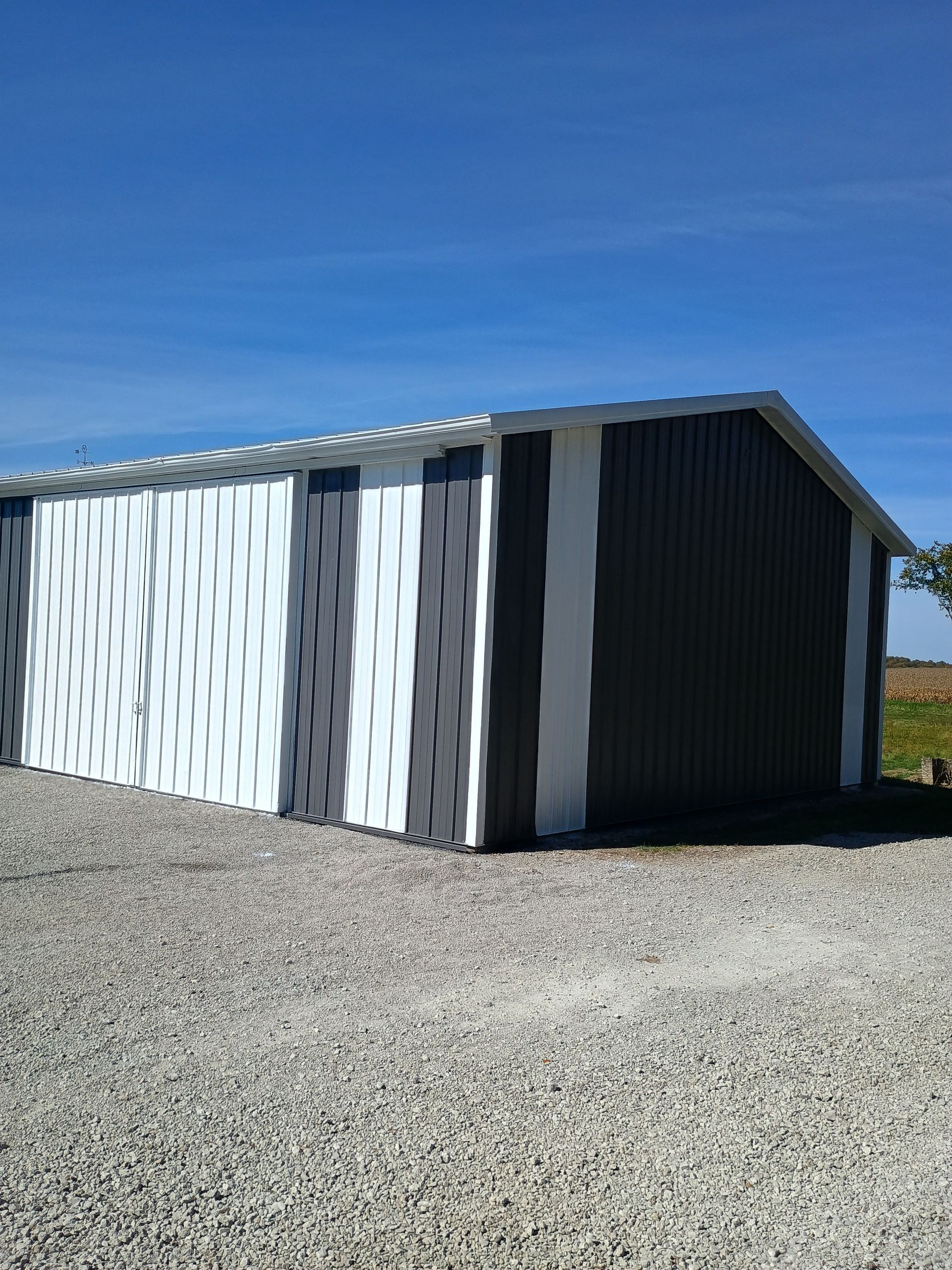 Small corrugated metal shed with white and dark gray sides on a gravel lot under a clear blue sky