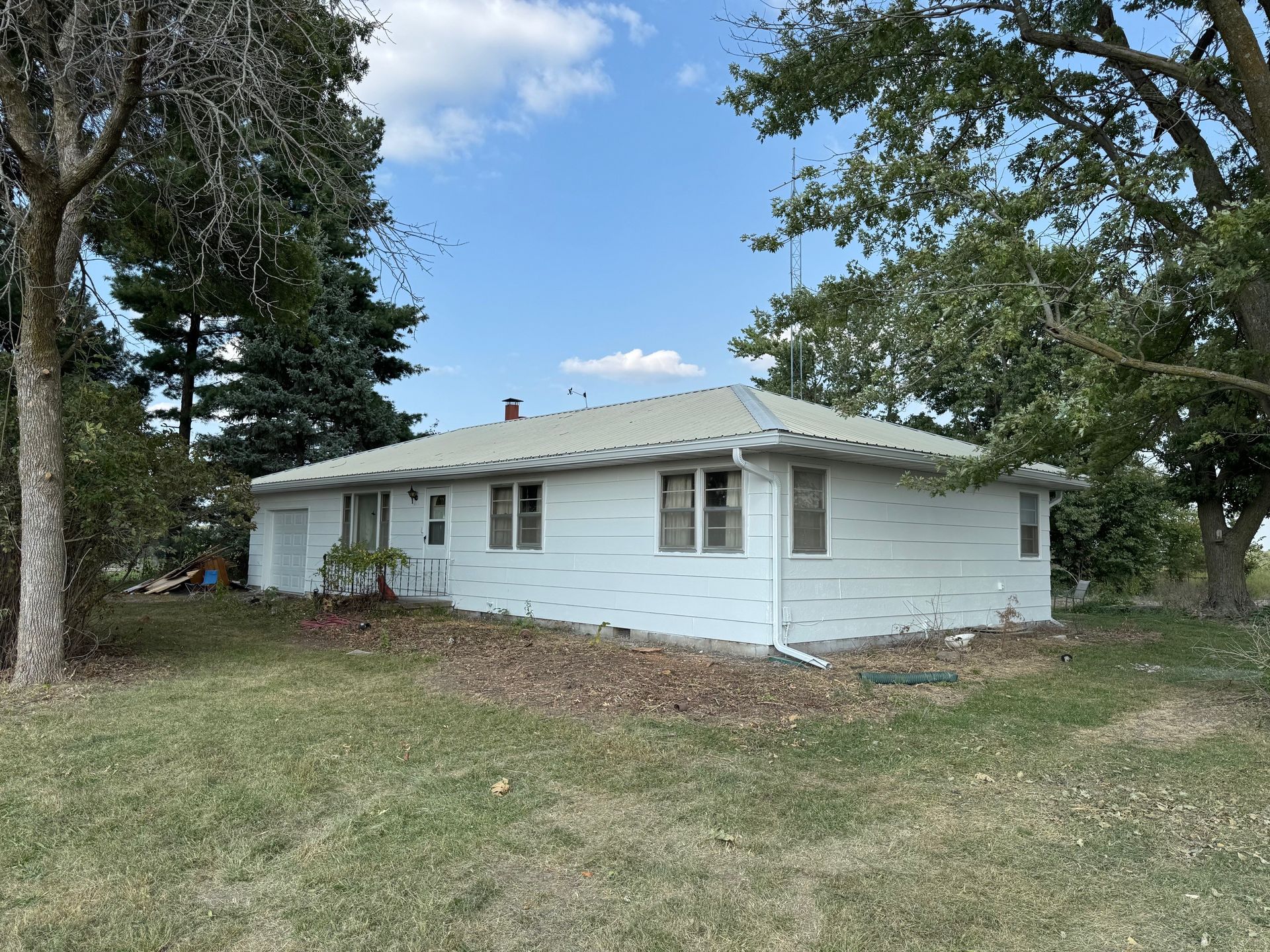 White single-story house with a metal roof and trees in a grassy yard under a blue sky