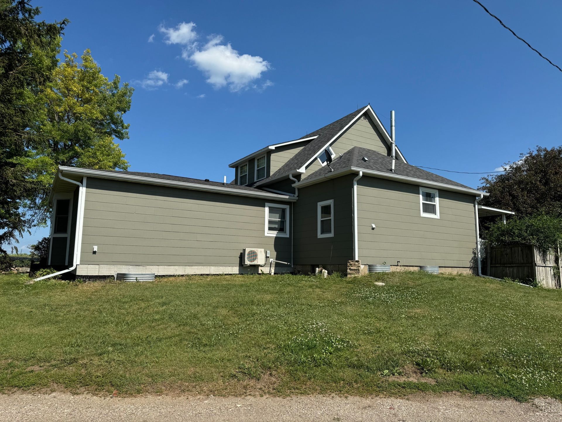 Gray house with white trim on a grassy hill under a blue sky with a few clouds