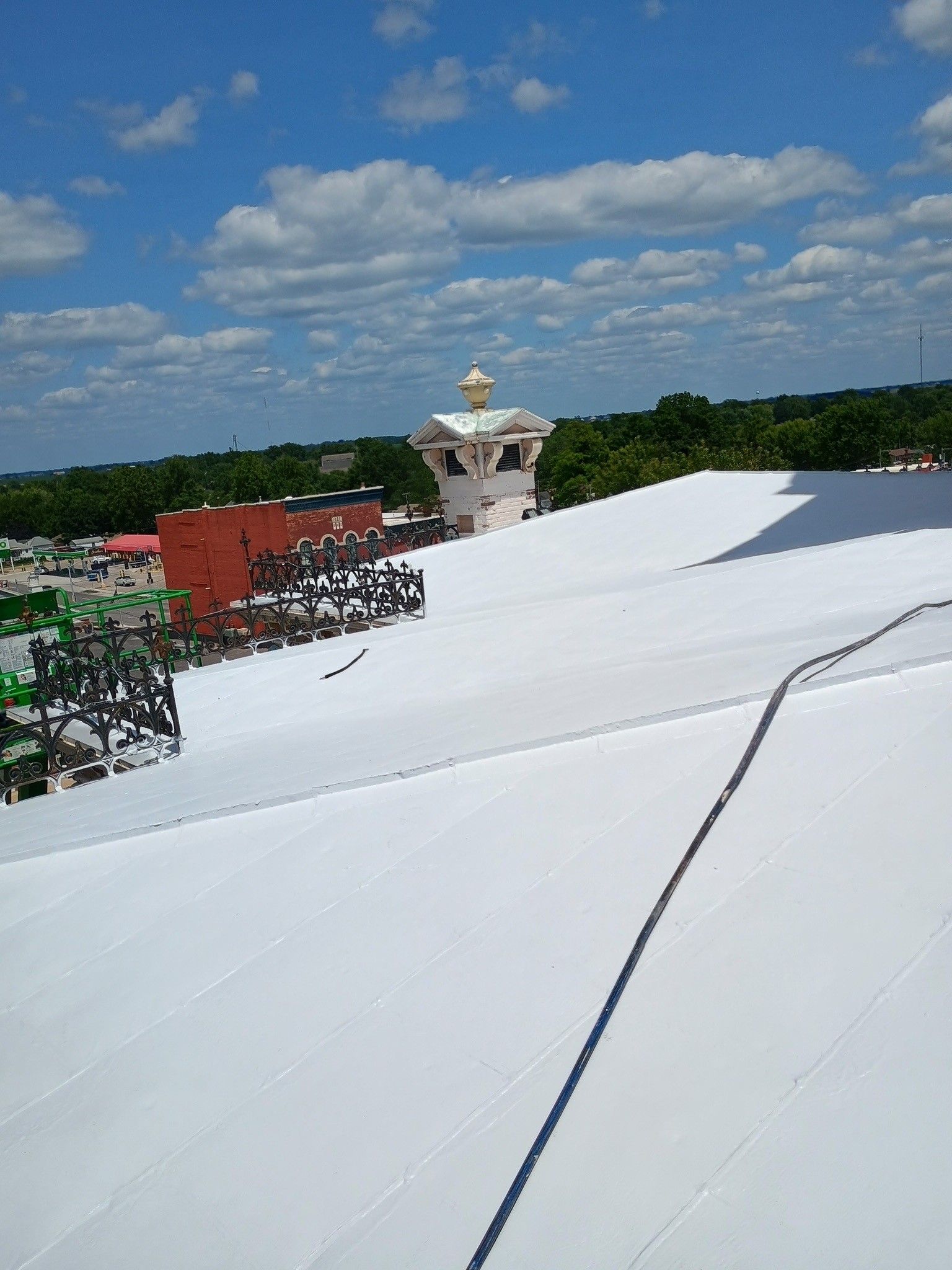 A high-angle view of a white, flat-roofed building under a blue sky, with a decorative structure in the distance.