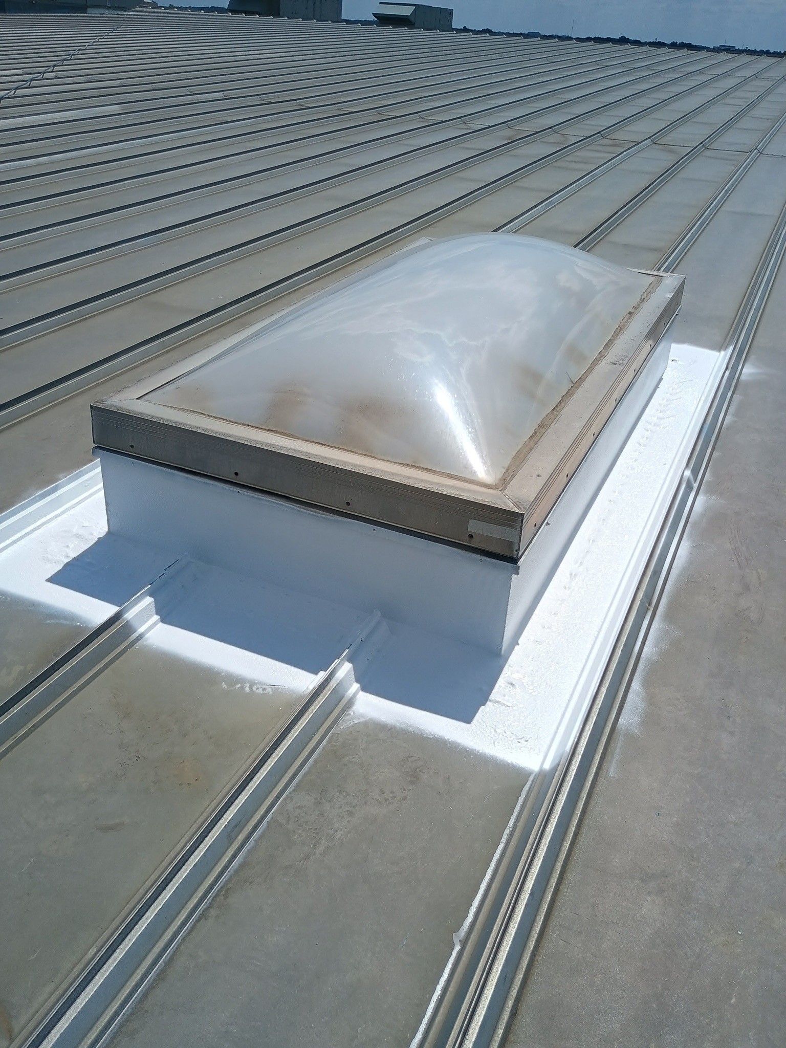 A rectangular skylight with a translucent bubble dome, sealed with white flashing on a ribbed metal roof.