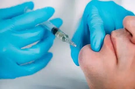 Gloved hands preparing to give a syringe injection into a person’s arm