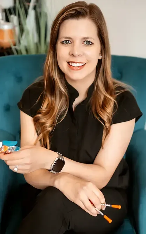 Smiling woman seated on a teal couch, holding orange sunglasses and a small colorful object
