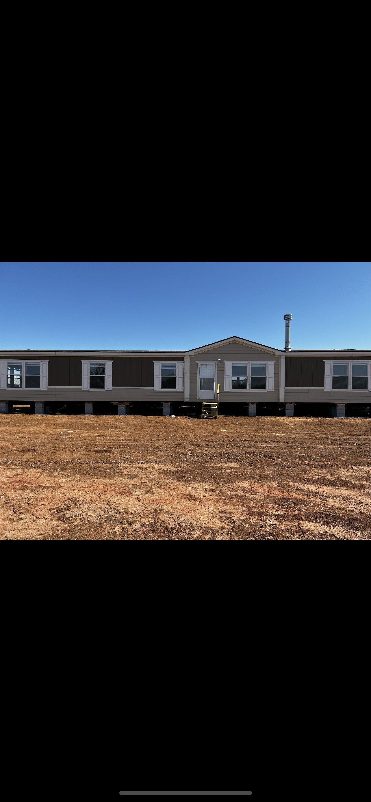 Gray and brown mobile home on blocks.