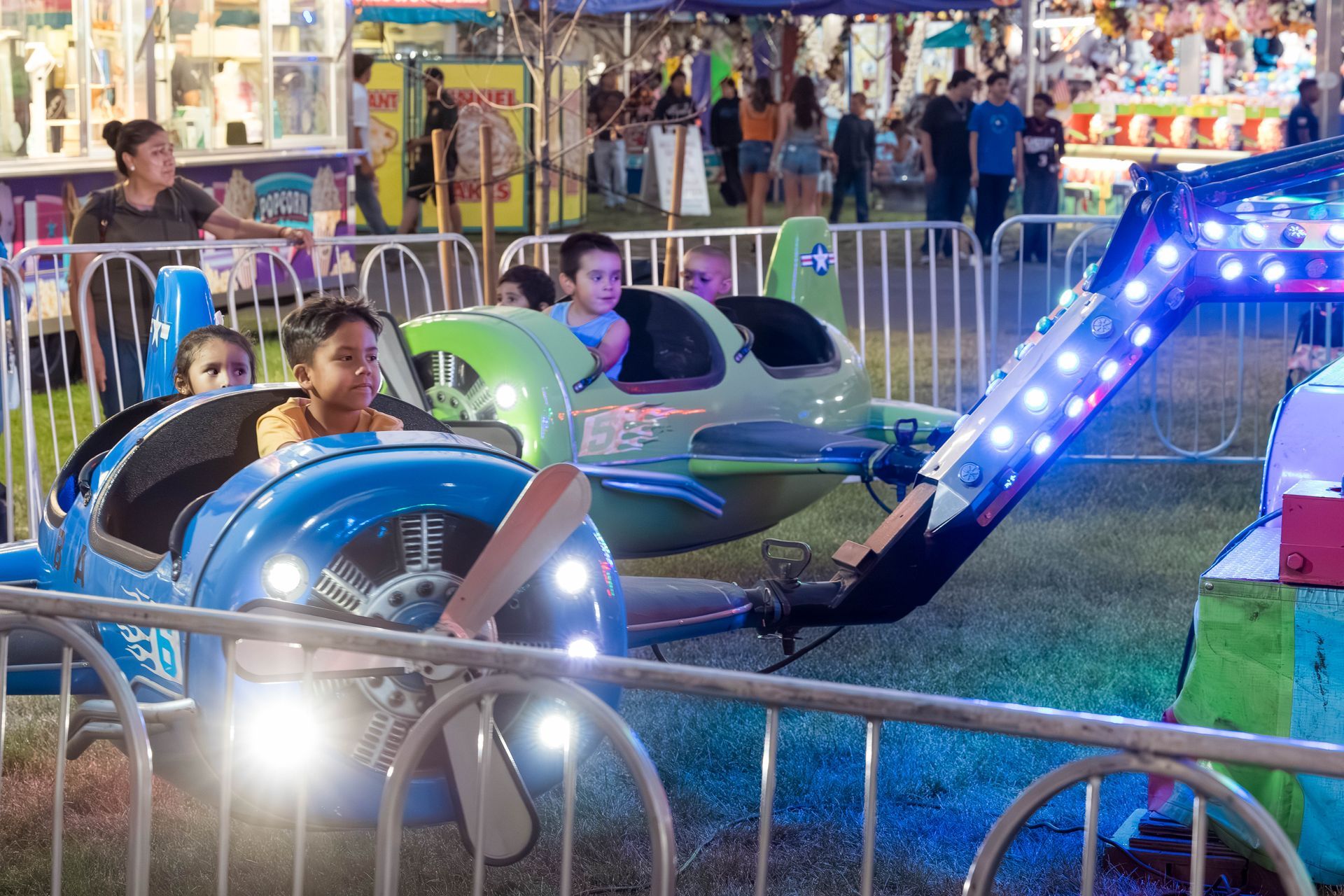 a little girl is riding a green airplane at a carnival